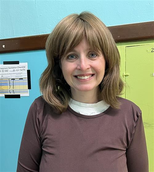 Teacher wearing a brown top and she is smiling.